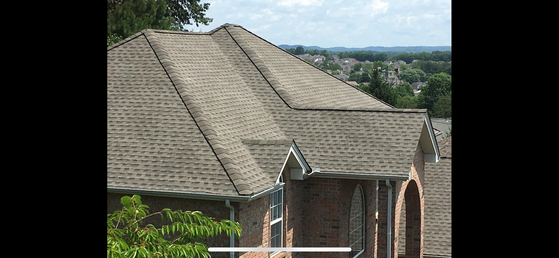 A view of a shingled roof on a brick house overlooking a neighborhood on a sunny day.