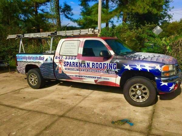 A Sparkman Roofing pickup truck wrapped in an American flag design with a ladder rack parked on a paved driveway.