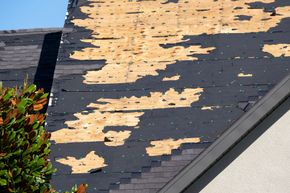 A section of a residential roof with missing shingles, exposing the underlying wooden roof decking.