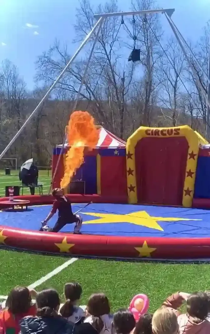 A group of children are watching a circus show on a field.