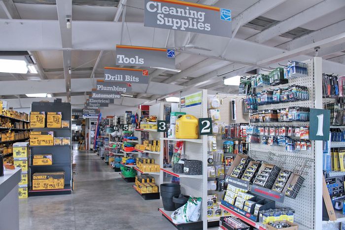 Hardware store aisle with tools, drills, and cleaning supplies on shelves and hanging signs