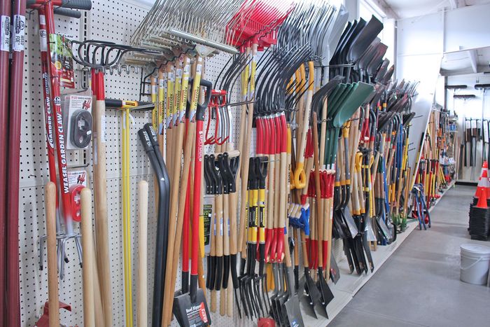Racks of garden tools and long-handled implements displayed in a hardware store aisle.