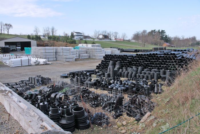 Piles of black pipes and fittings stored outdoors on a construction site under an overcast sky