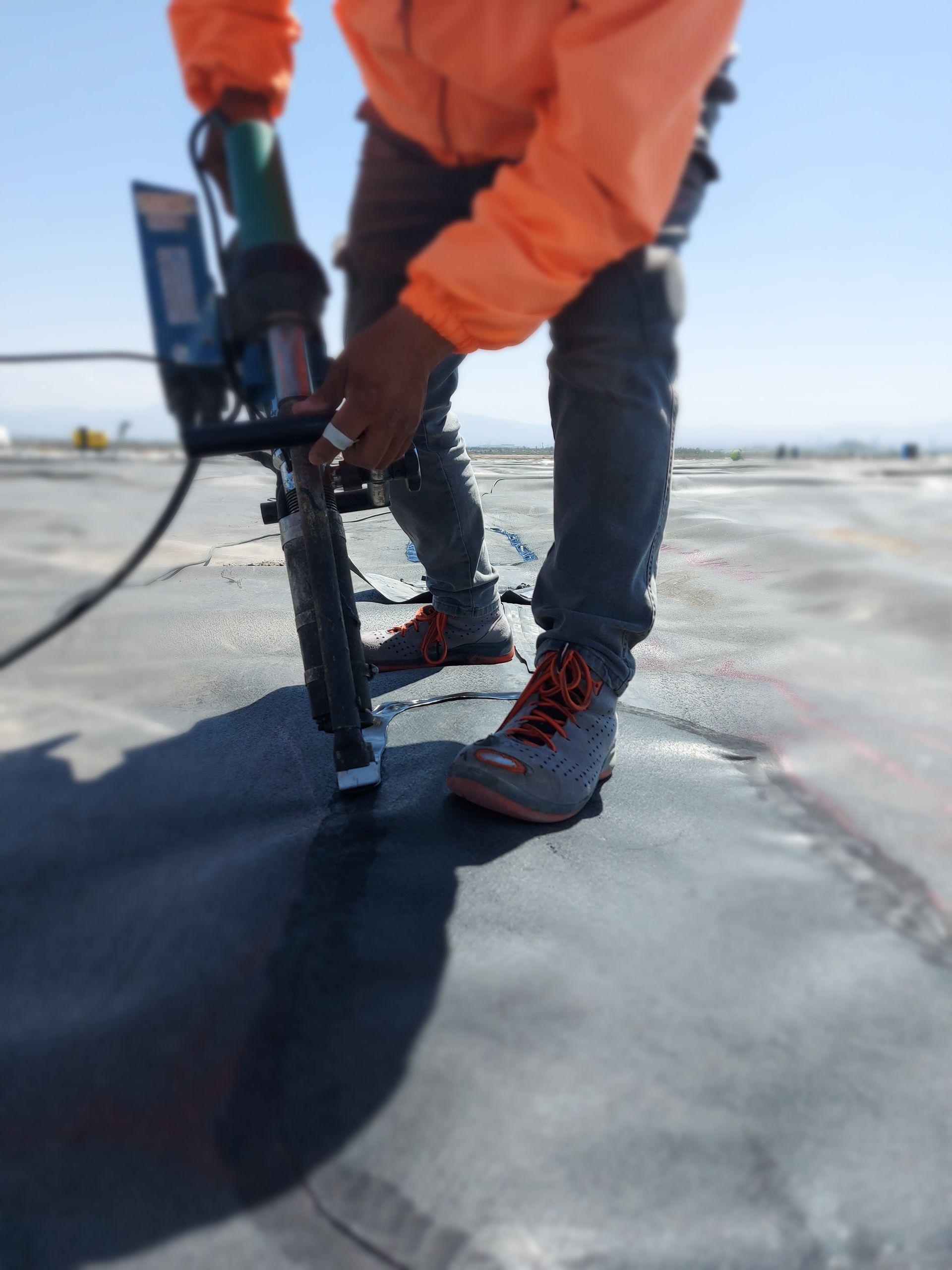 Person in orange jacket using a tool on a dark surface outdoors.