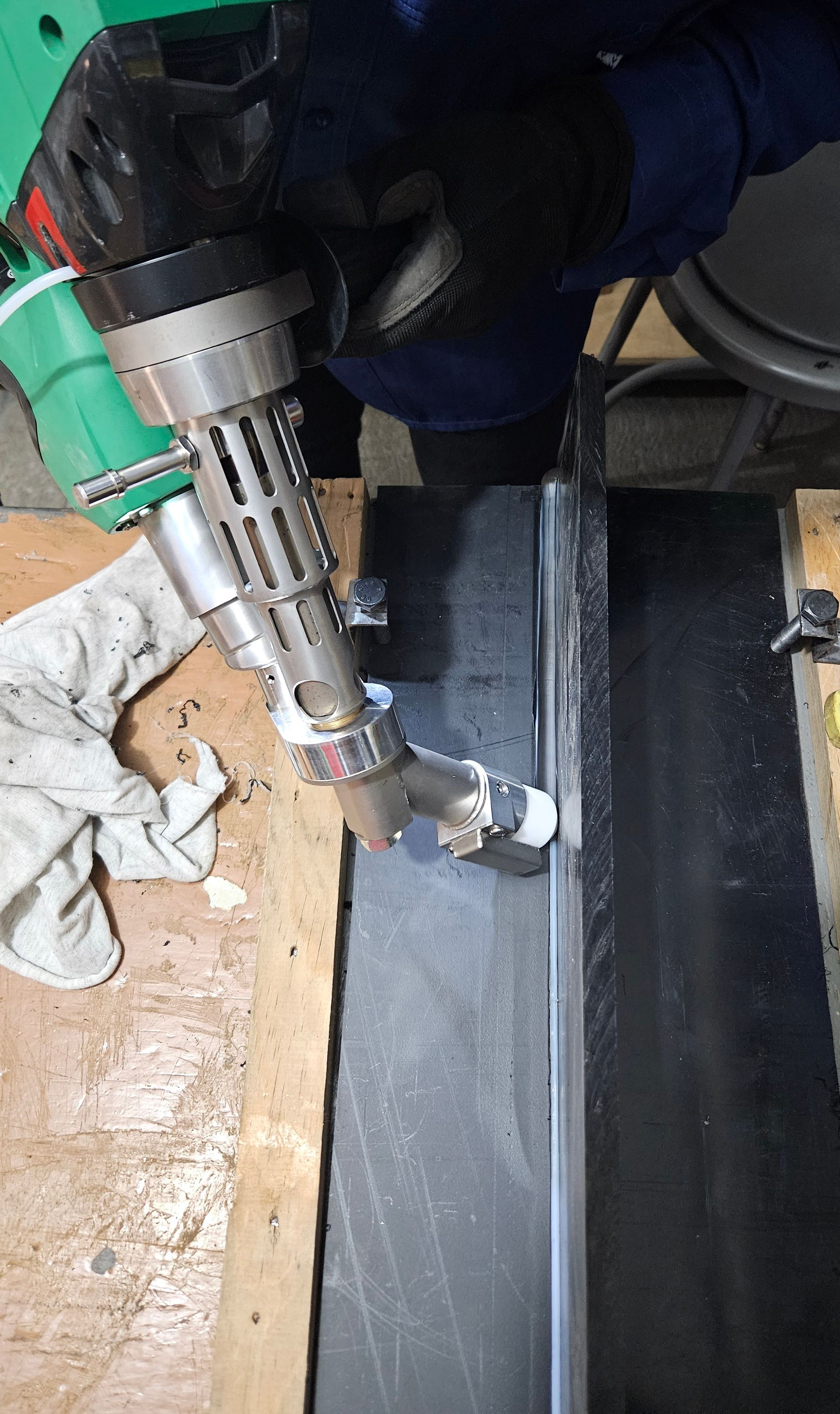 Person welding a dark-colored surface with a handheld welding tool in a workshop setting.