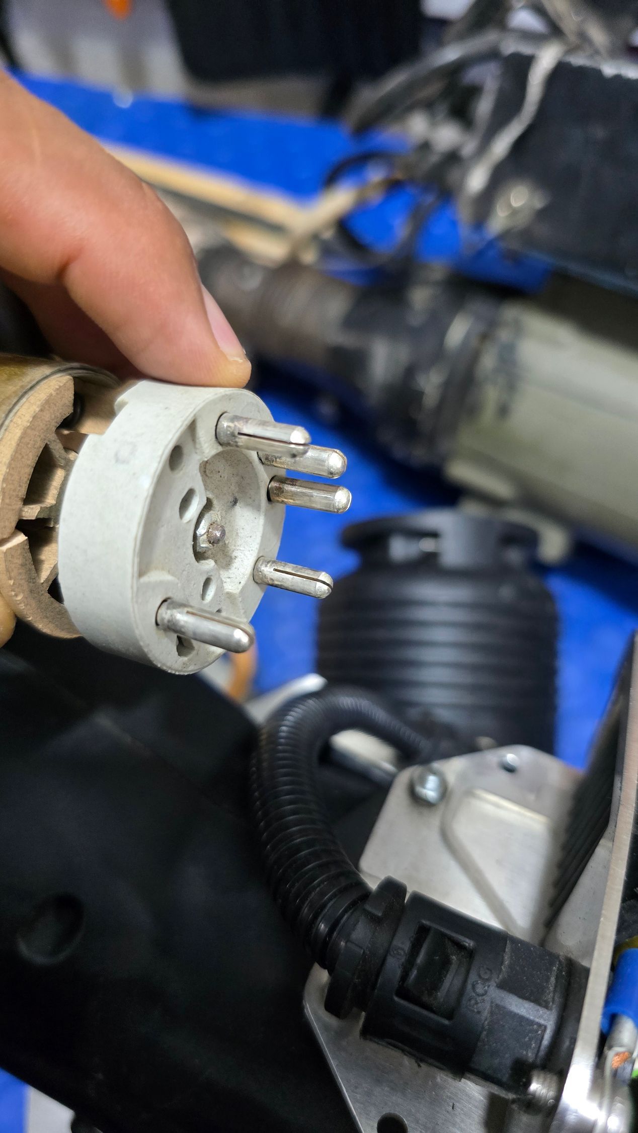 A hand holds an electrical component with multiple pins. Black wiring and other parts are in the background.