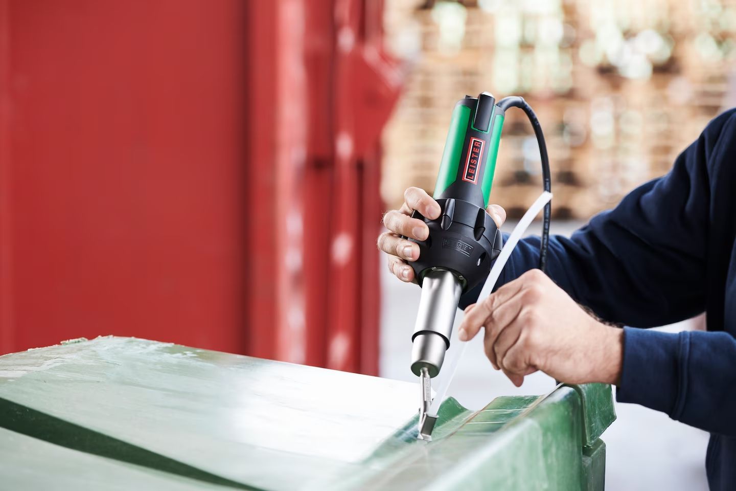 Person using a handheld welding tool on a green plastic container, indoors.