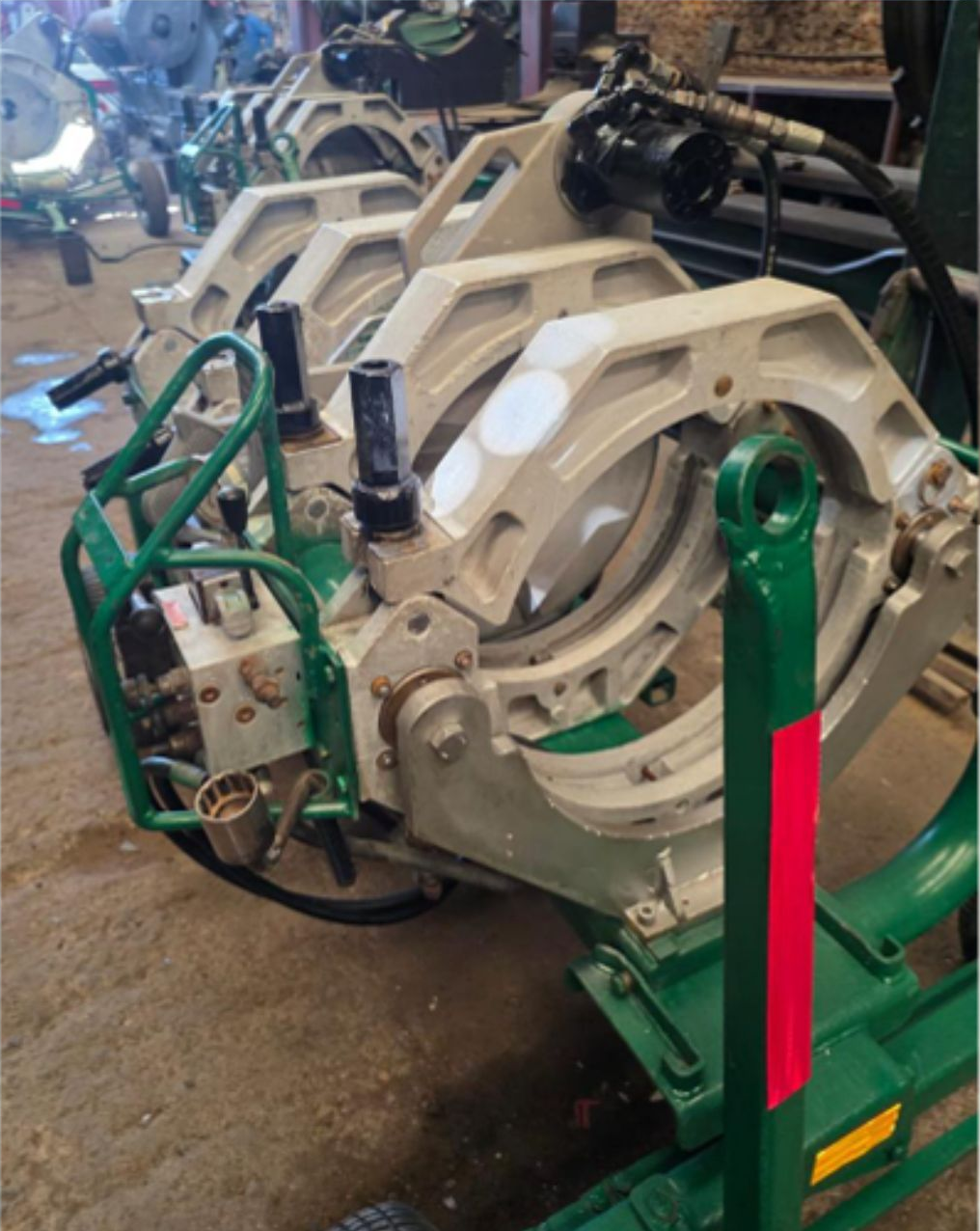 Large green and beige pipe fusion machine. Indoors, heavy-duty industrial equipment.