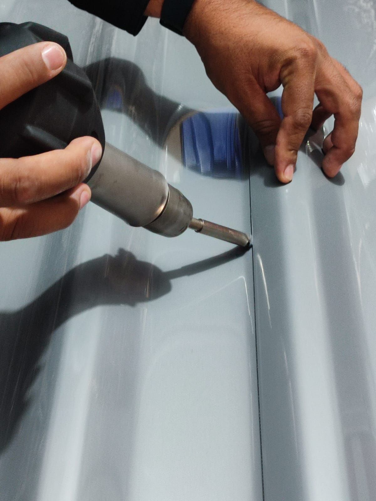 Person using a drill to connect two gray corrugated metal sheets.
