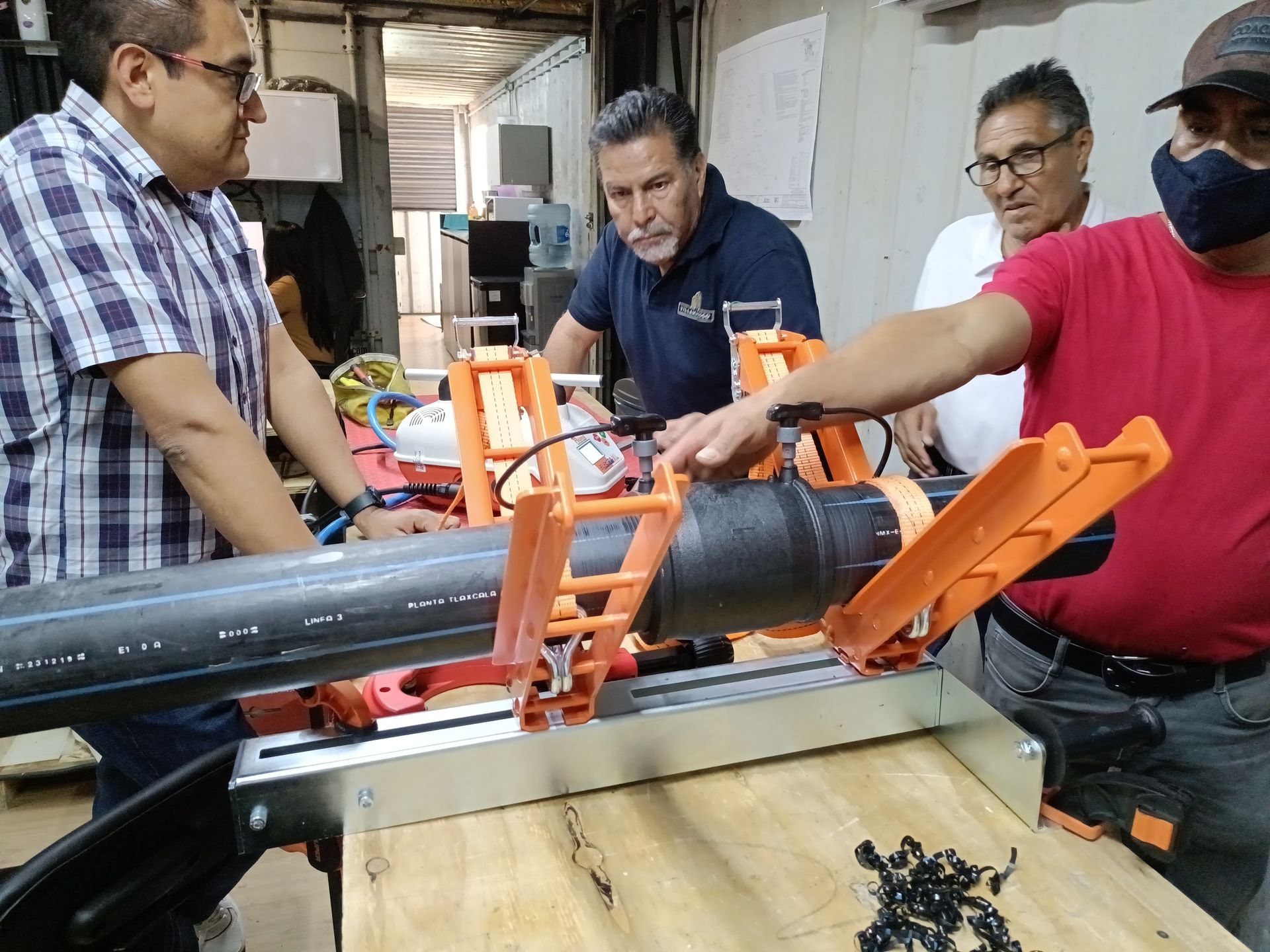 Men examining a cutting tool for pipes in a workshop. One man points at the tool.