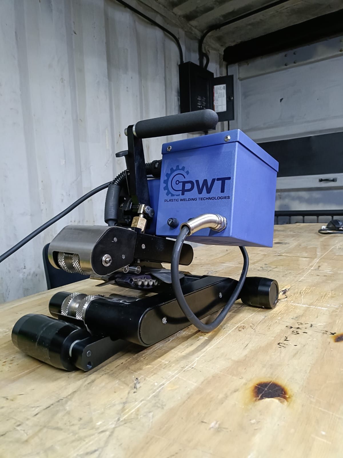 Black and blue portable welding machine on wooden surface. It has a handle and is labeled "PWT".