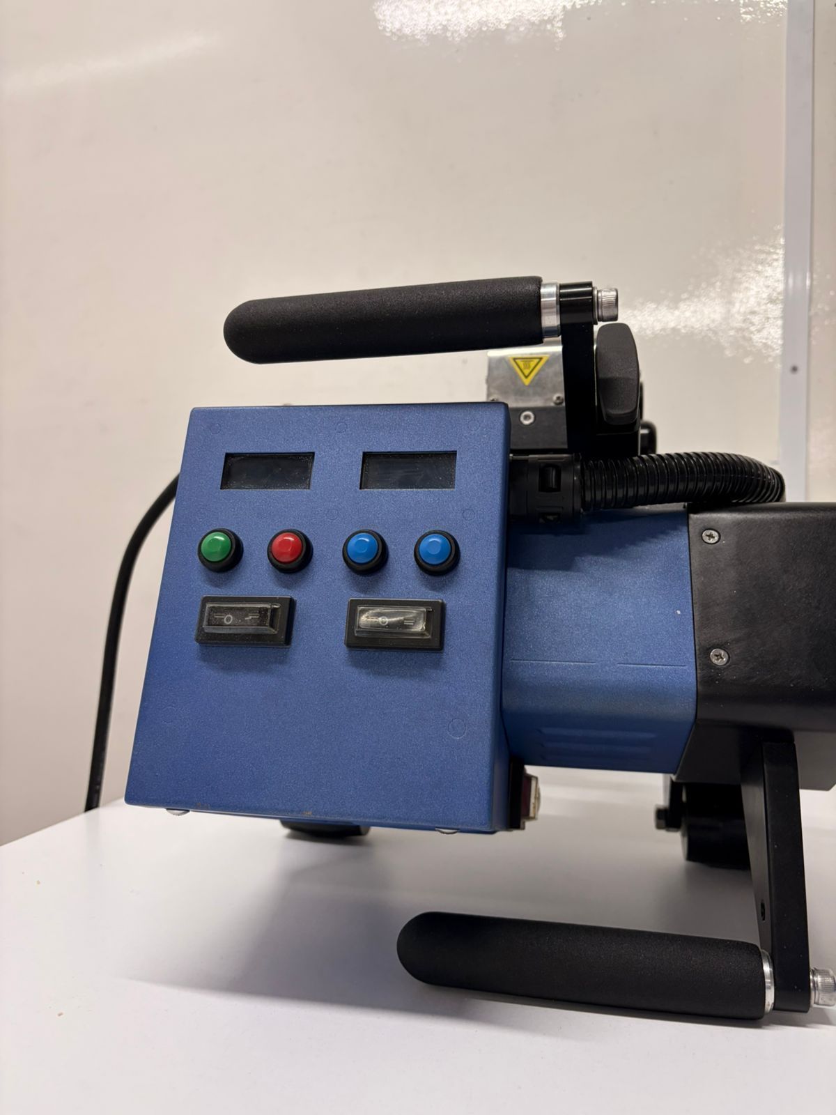 Blue industrial machine with black handles and red, green, and blue control buttons on a tabletop