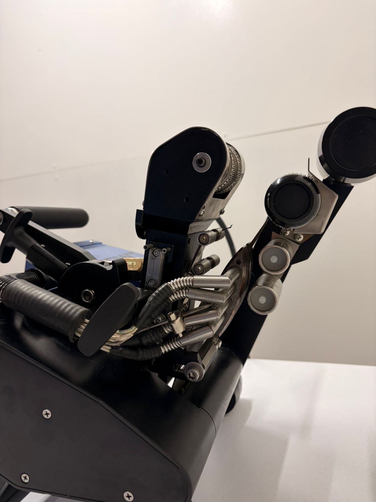 Black robotic hand with articulated fingers on a tabletop, shown against a plain light background.