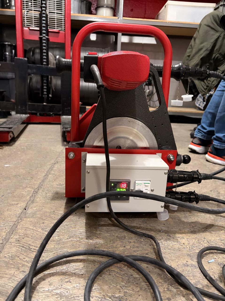 Red and white industrial pipe saw with attached power cables, indoors.