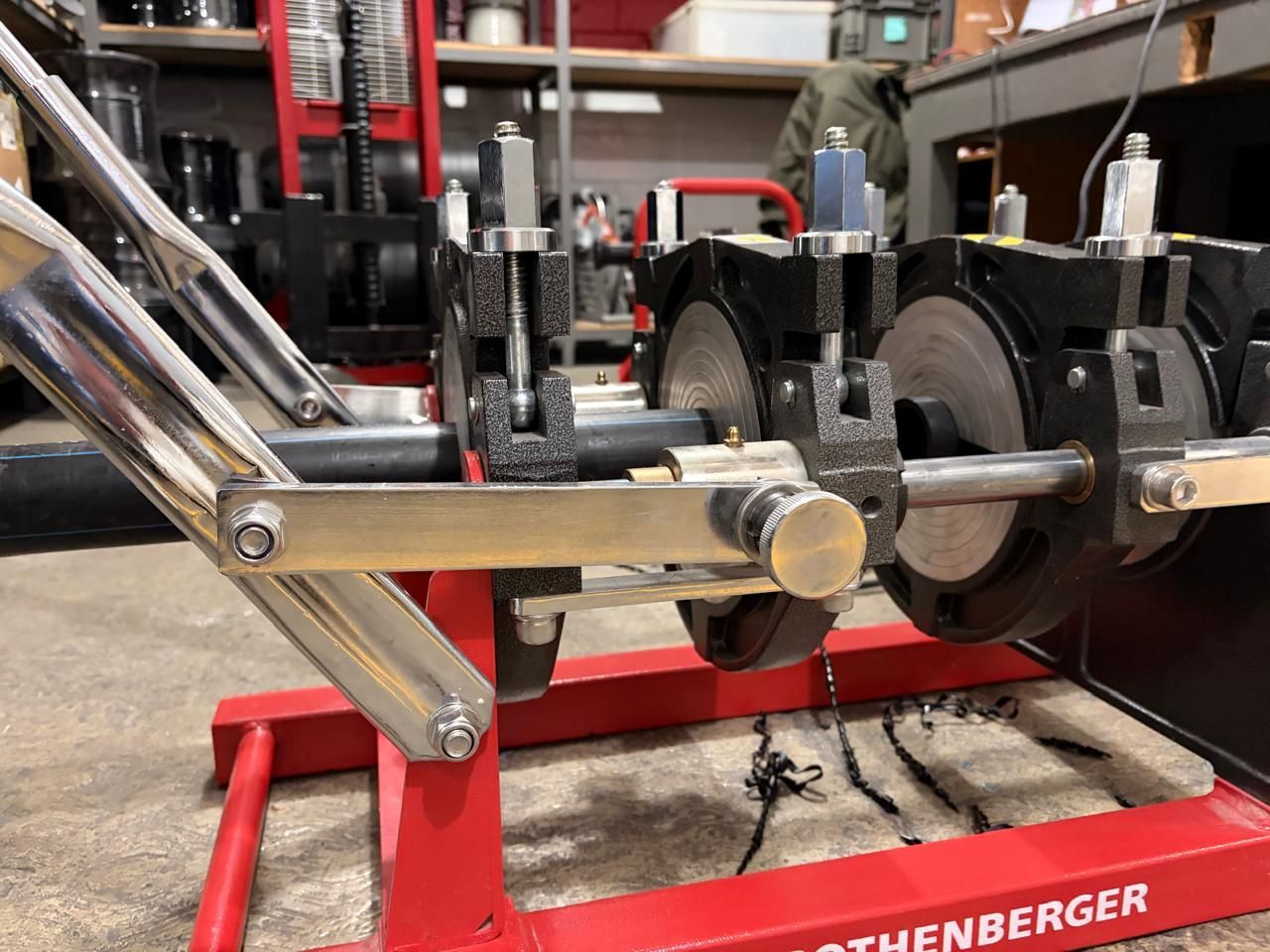 Plumbing tool on a red stand welding pipes together. Silver pipes and parts, dark metal, and a gold knob.