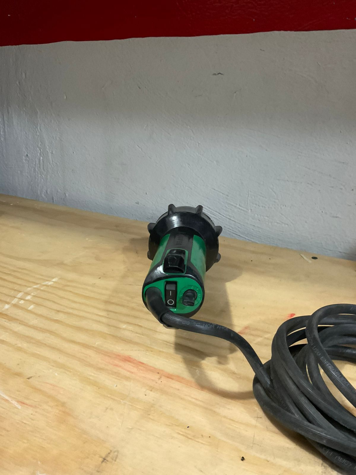 Green and black heat gun with coiled power cord on a wooden surface.