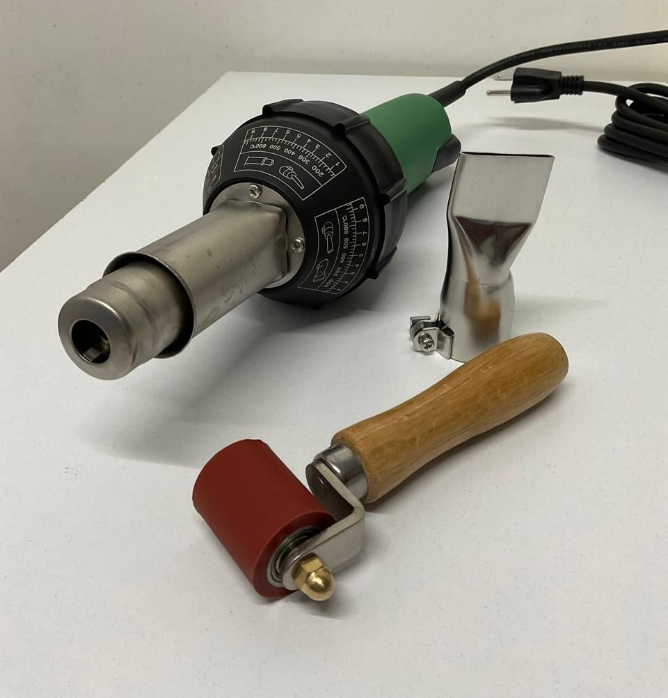 Heat gun with two wooden-handled rollers and a metal scraper on a white surface