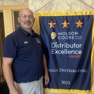 Man standing beside a blue Molson Coors Distributor Excellence Award banner, 2023.