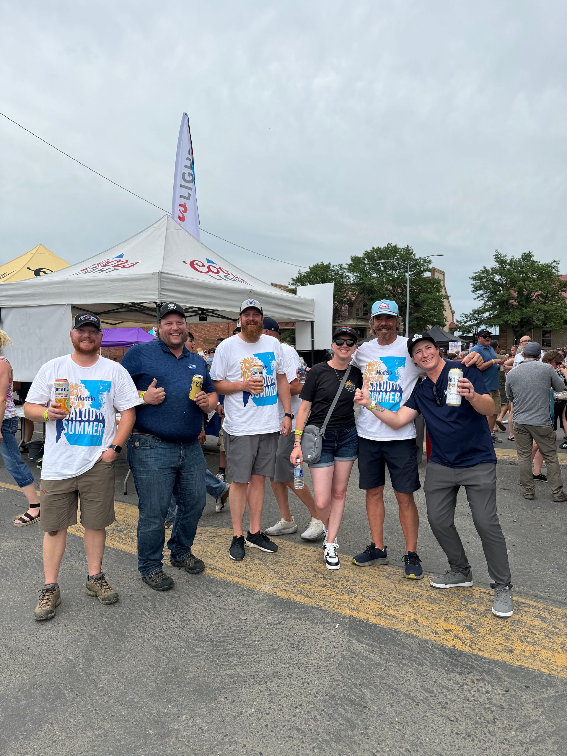 Group of volunteers in white event T-shirts posing outdoors near a white tent on a cloudy day
