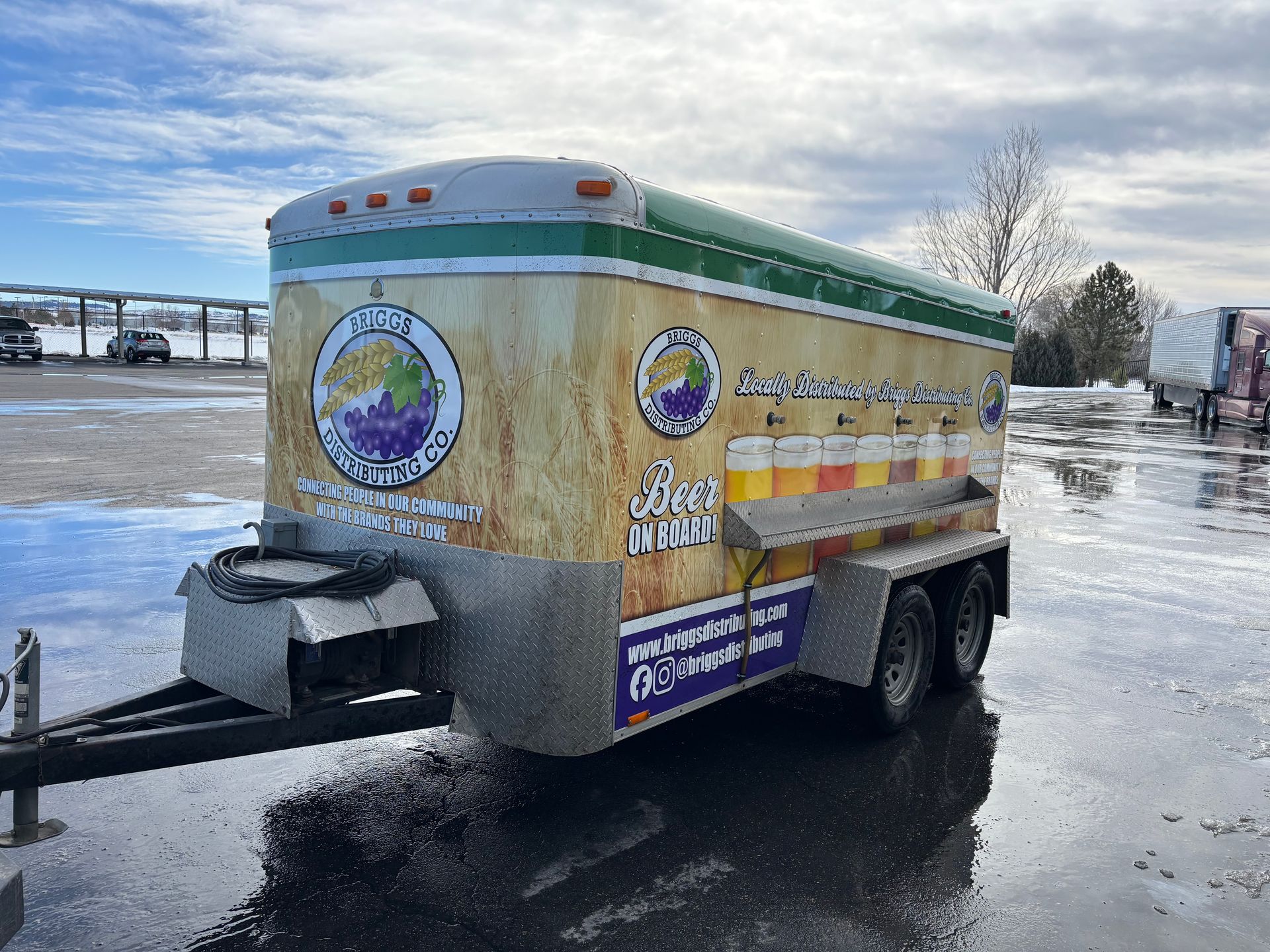 Snowy trailer with colorful circular logos parked outdoors on a wet lot