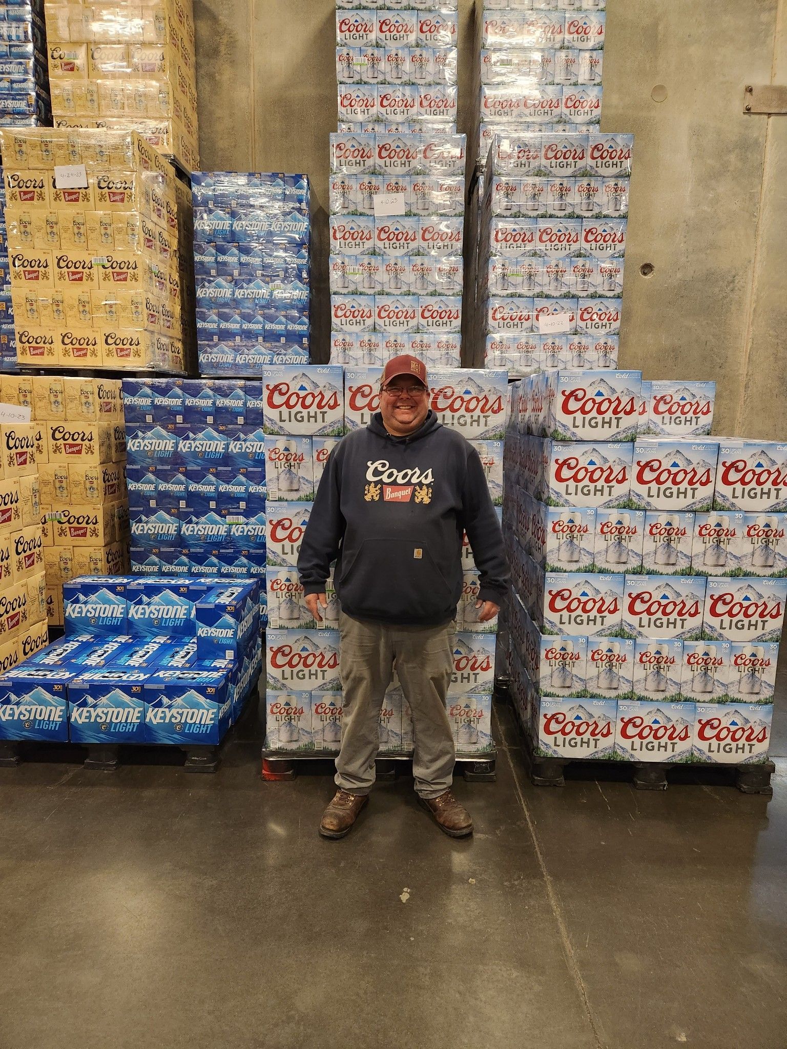 Man standing in front of stacked beverage boxes and cases in a warehouse aisle