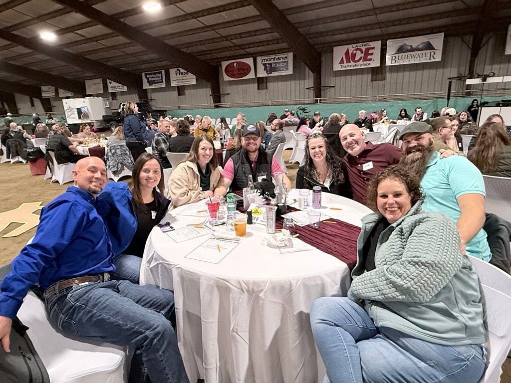 Group of people seated at a round table in a crowded indoor banquet hall, smiling at the camera.