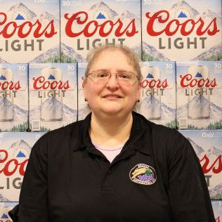 Woman in a black polo standing before a Coors Light backdrop, smiling at the camera.