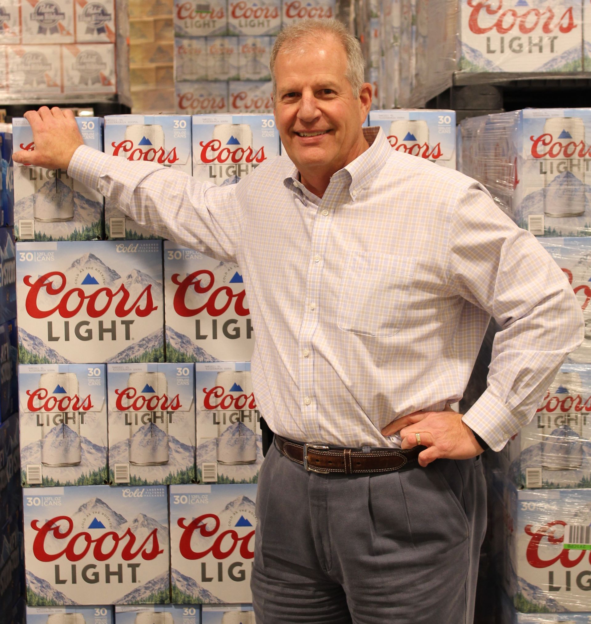 Man posing in front of stacked Coors Light boxes, hand on one box and smiling