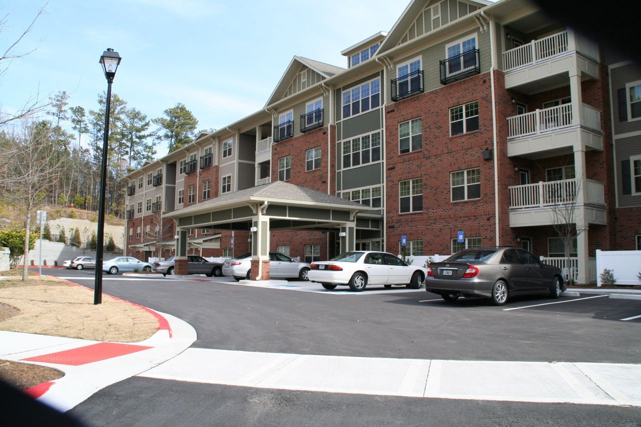 Exterior view of a multi-story apartment building with a covered entrance and a paved driveway.