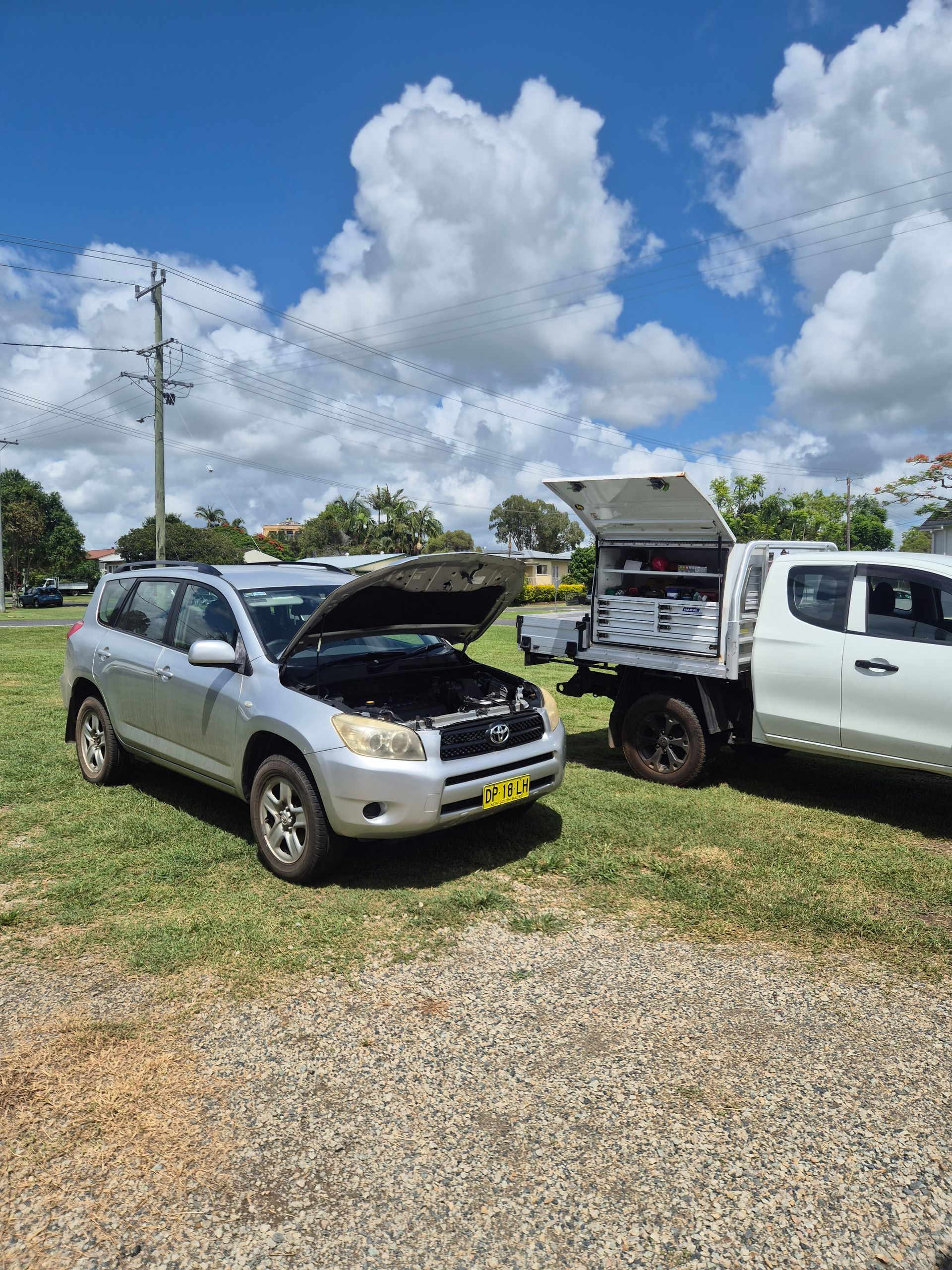 A silver SUV with its hood raised is parked on grass next to a white utility truck — Exceed Onsite Mechanical in Grafton, NSW