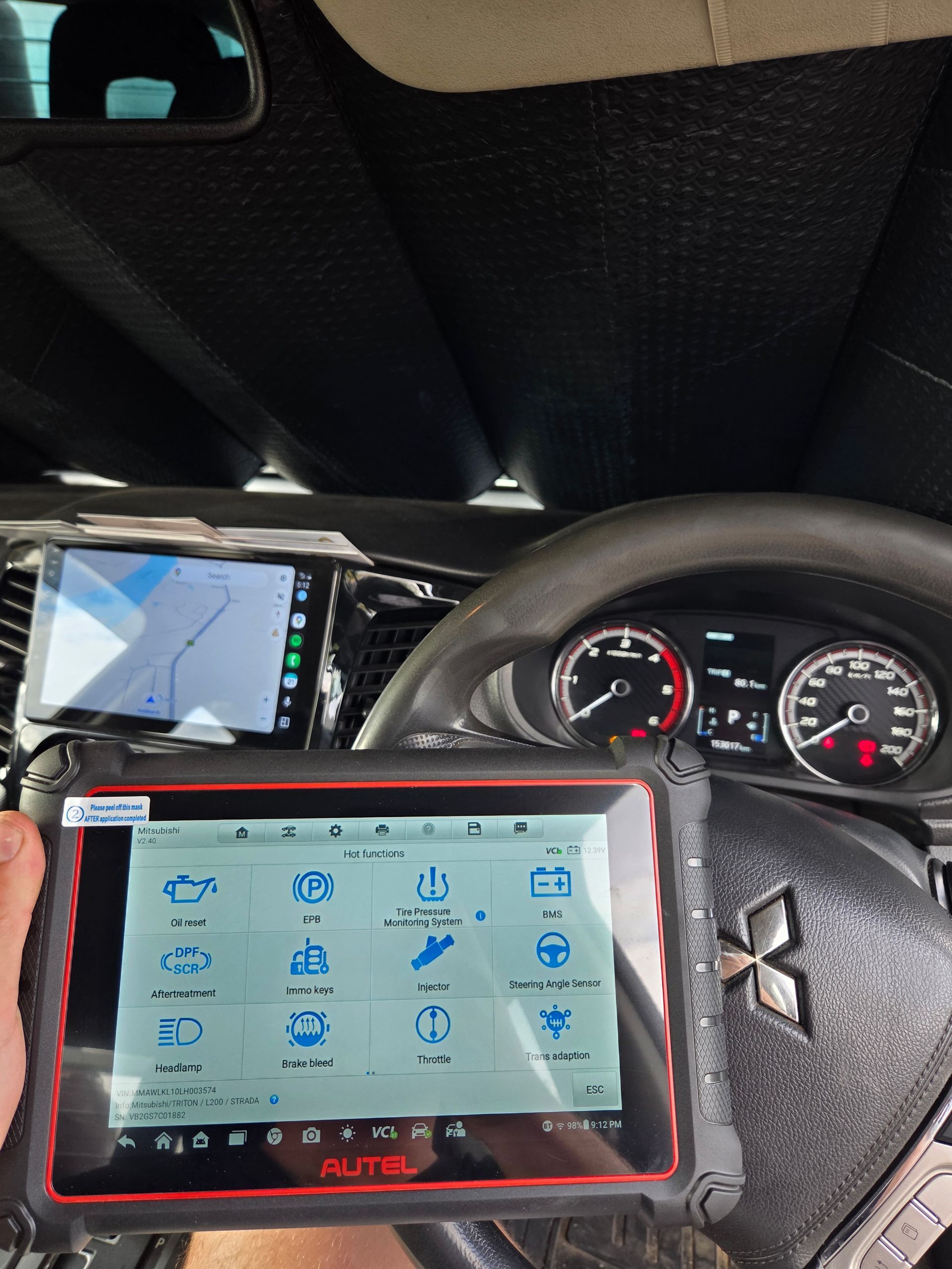 A diagnostic tablet displaying service icons held in front of a Mitsubishi steering wheel — Exceed Onsite Mechanical in Grafton, NSW