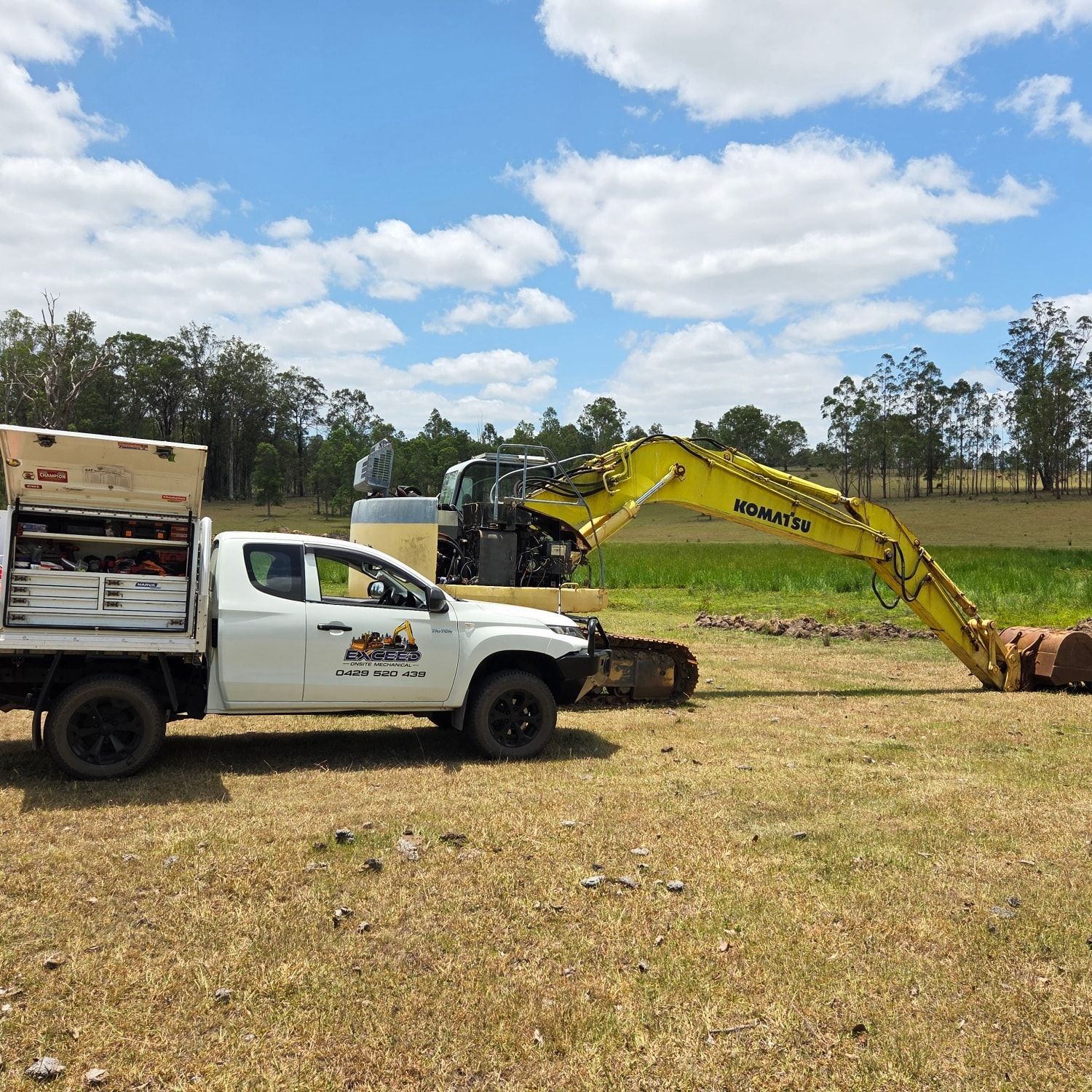 A White Service Truck Parked on Dry Grass Next to A Yellow Kobelco Excavator — Exceed Onsite Mechanical in Grafton, NSW