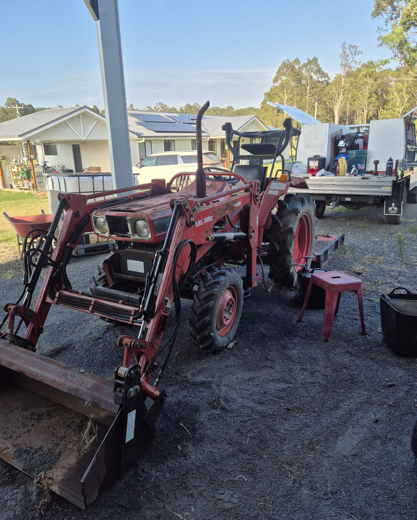 A Red Tractor with A Front Loader Sits on A Gravel Driveway in Front of A House — Exceed Onsite Mechanical in Grafton, NSW