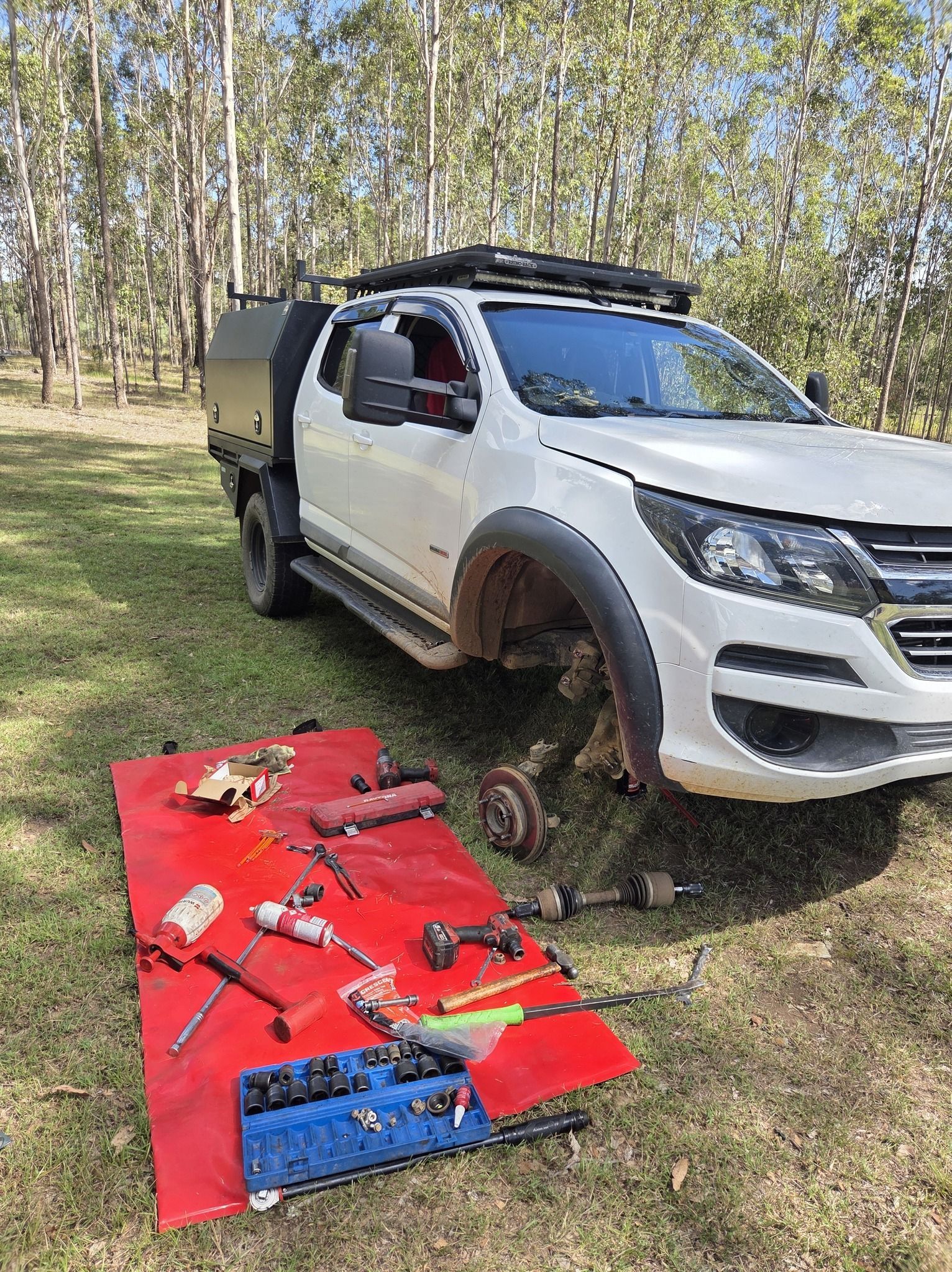 A Pickup Truck with A Missing Front Wheel with Tools and Parts Spread on A Red Mat — Exceed Onsite Mechanical in Grafton, NSW