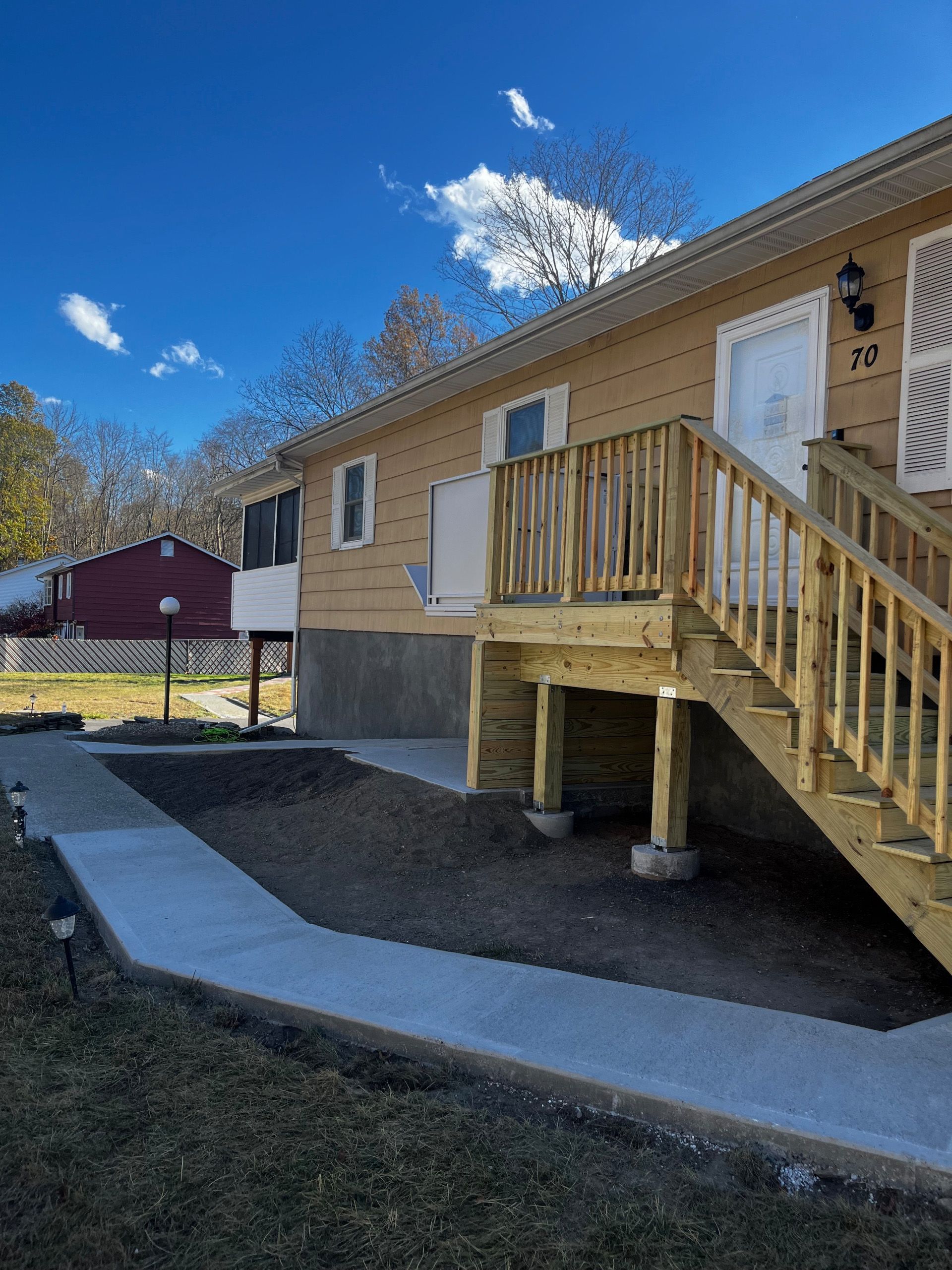 A two-story tan building with wooden deck and stairs. Concrete pathway leading to entrance. Bright blue sky.