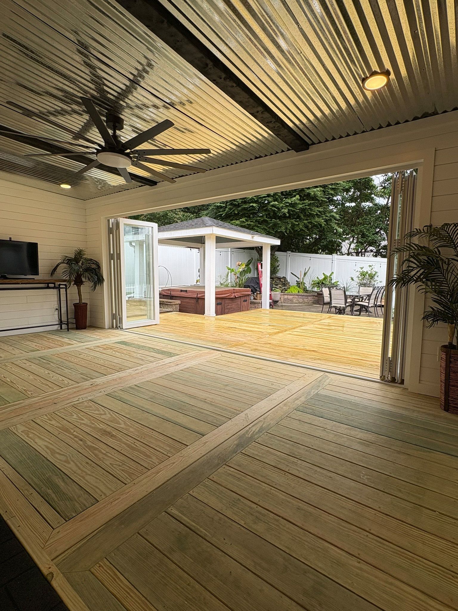 Patio with bi-fold doors open to a sand area. Outdoor ceiling fan, white walls, wooden floor.