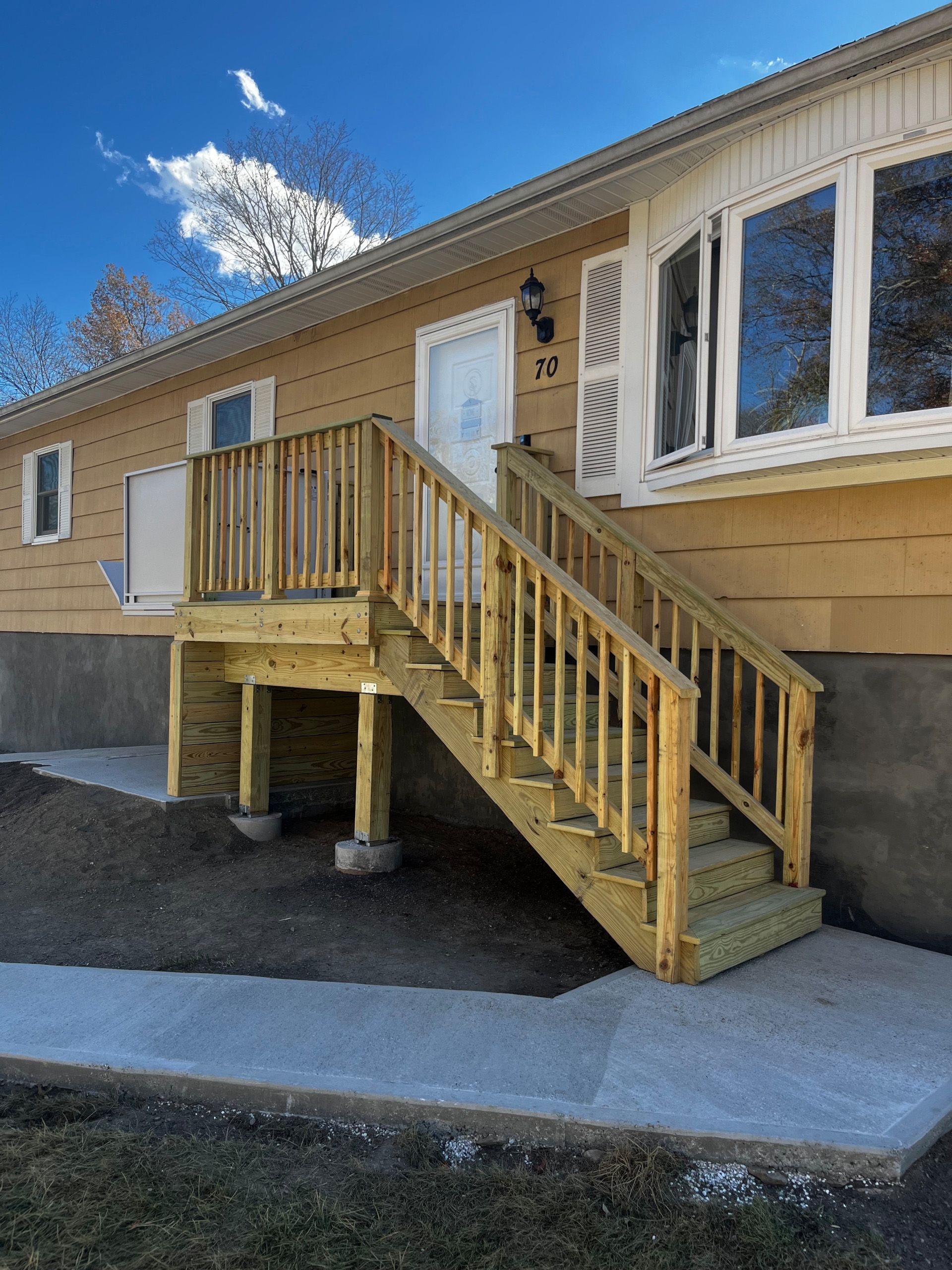 Wooden deck with stairs leading up to a tan house with a bay window and white door.