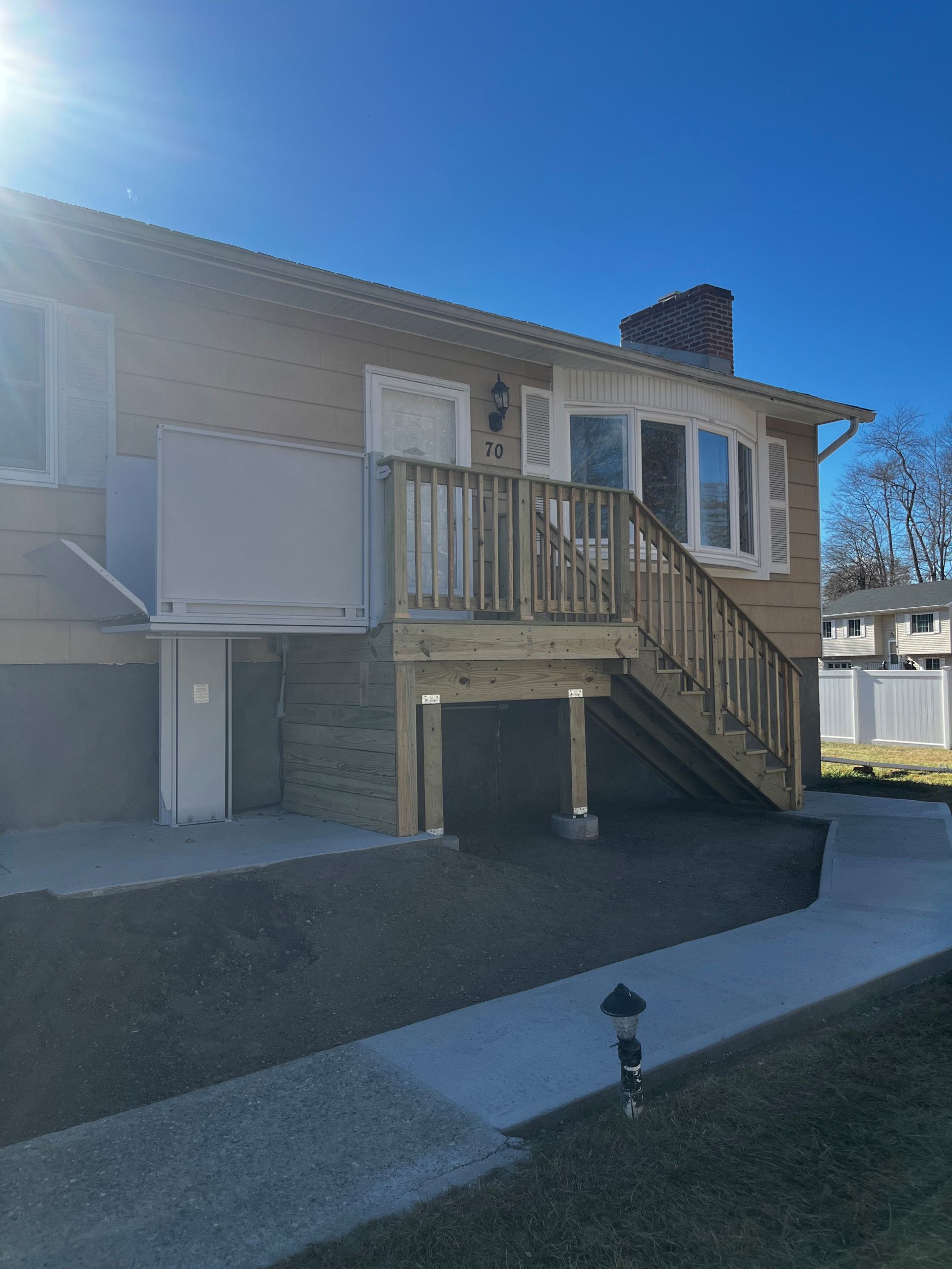 A light brick house with wooden deck, stairs, and lift; sunny day.