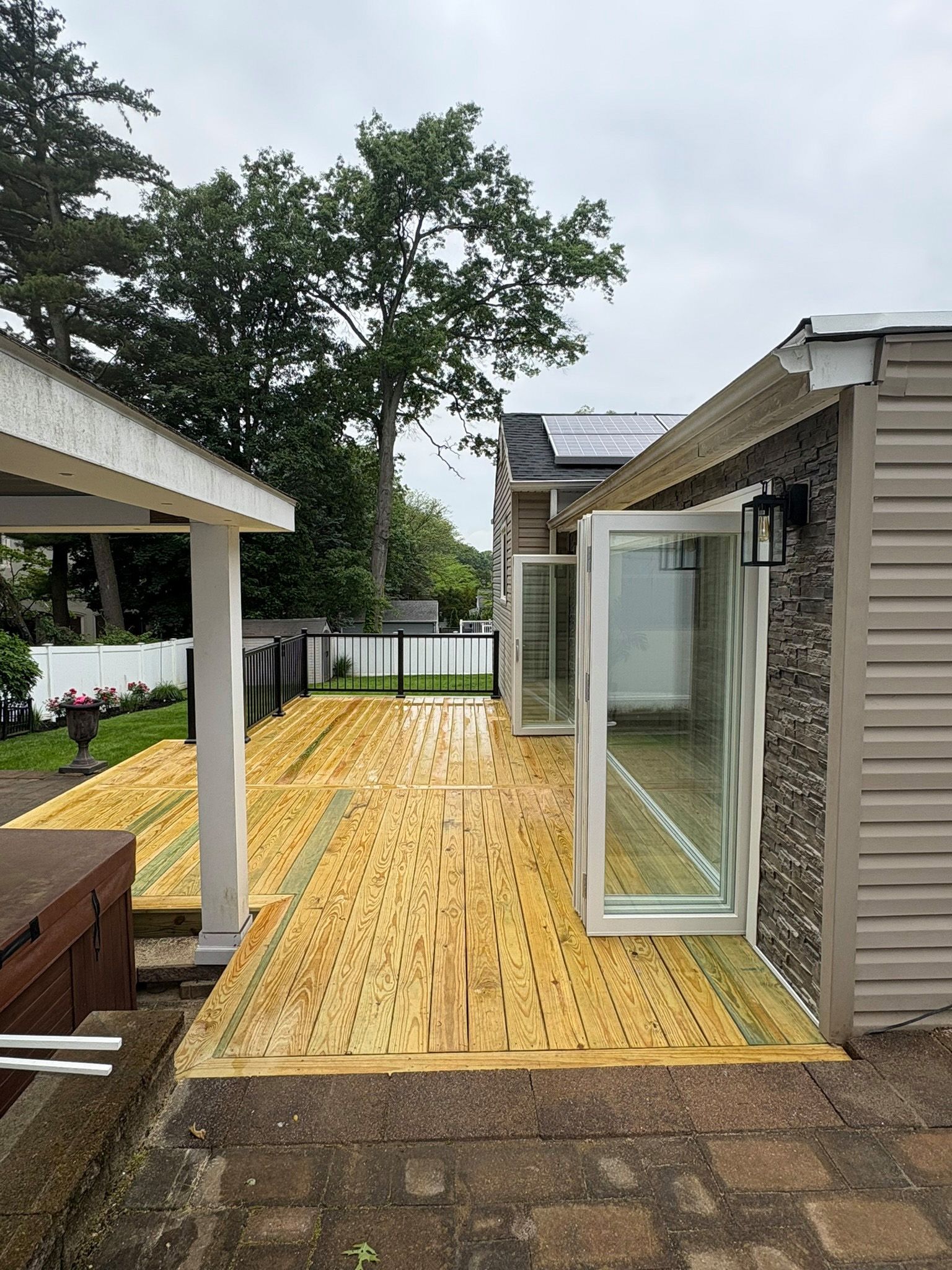 Wooden deck with folding glass doors leading to a stone-walled building.