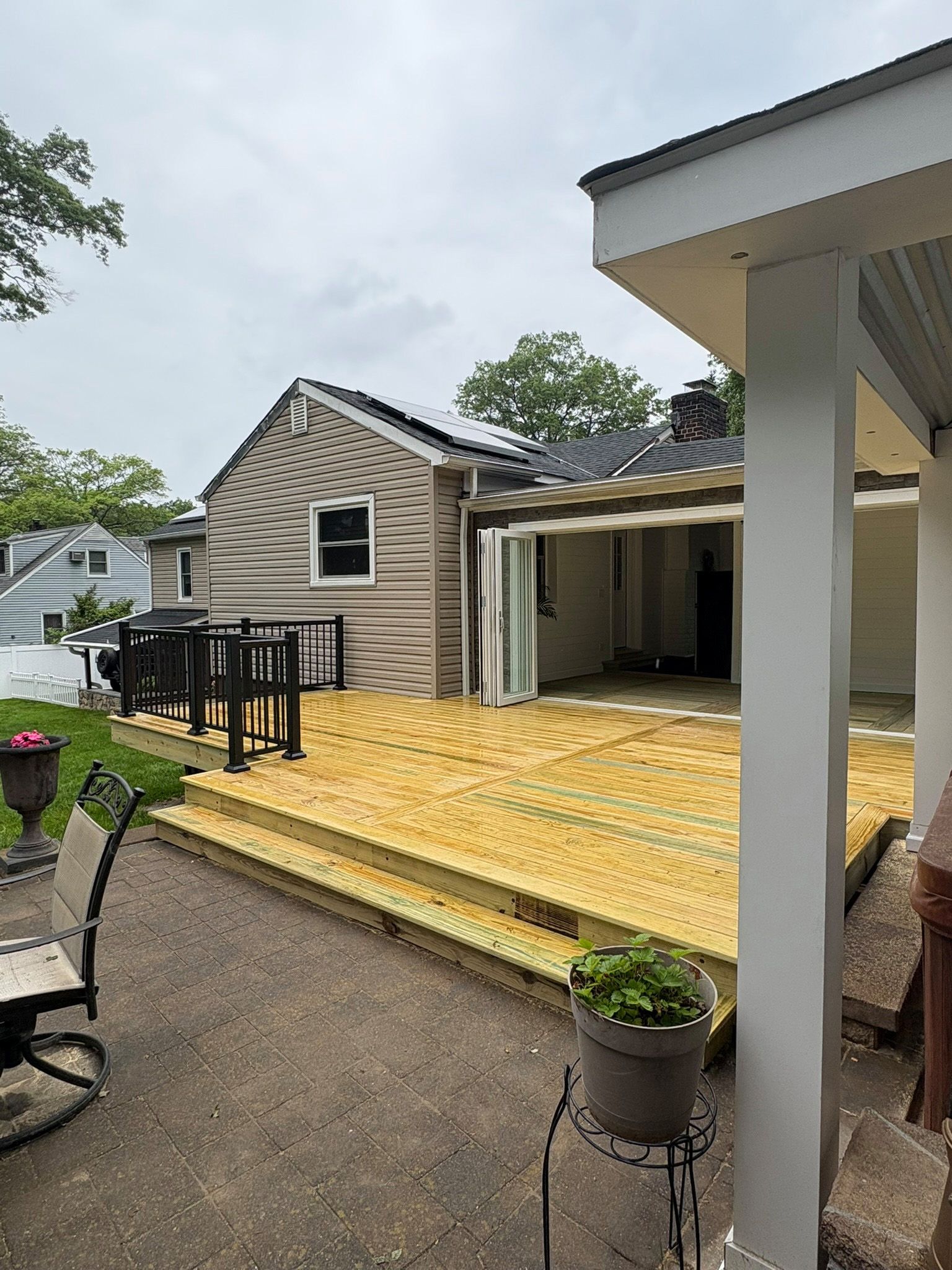 Wooden deck with a house in the background and a covered patio to the right. Cloudy day.