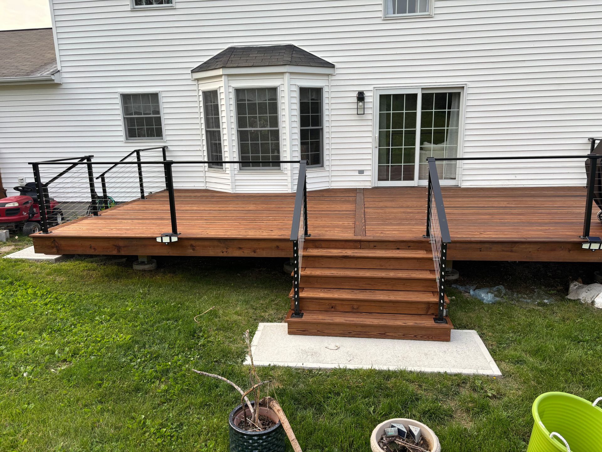 Wooden deck with stairs and black metal railing, set against a white house with a sliding glass door.