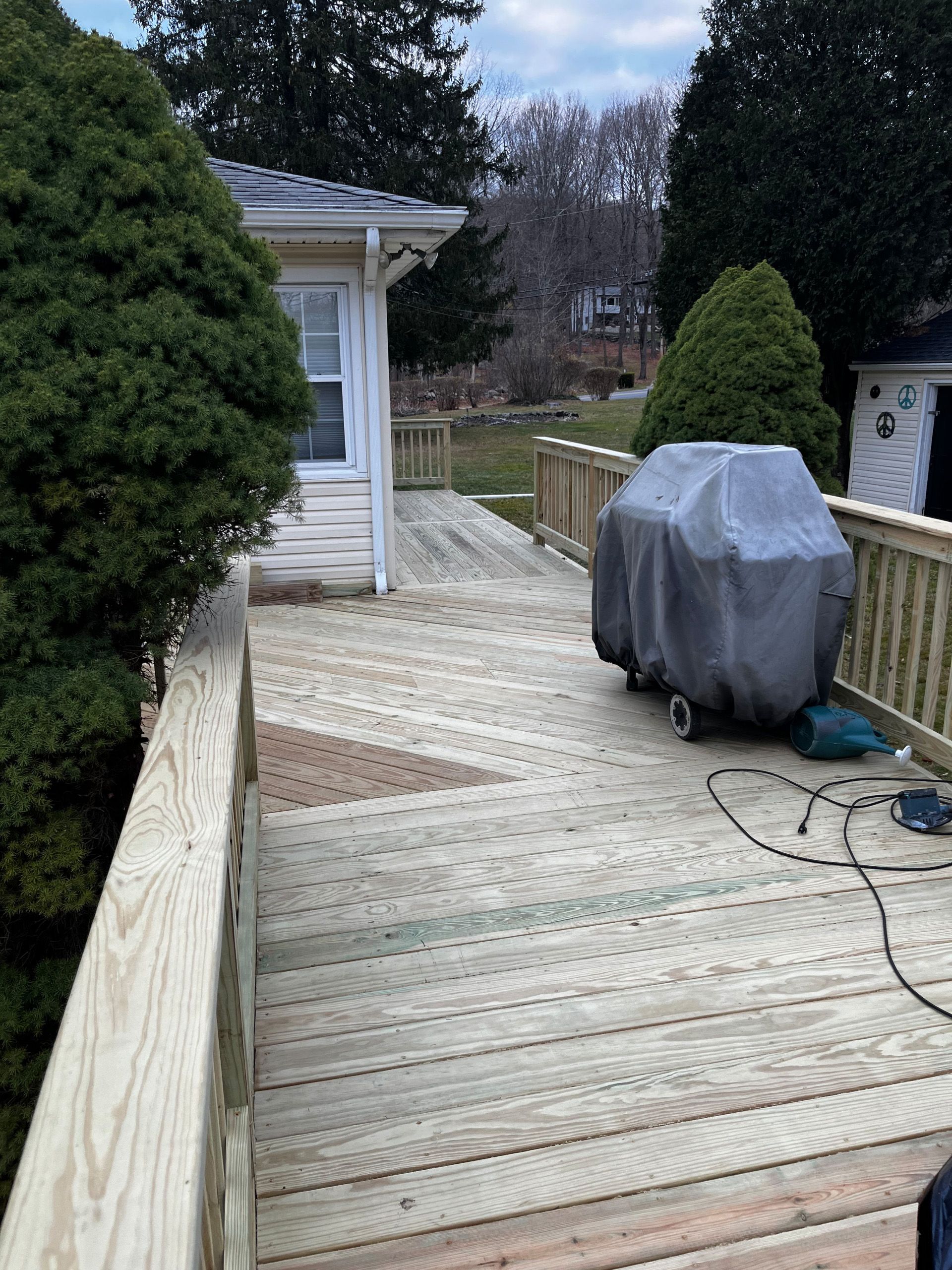 Wooden deck with a covered grill, adjacent to a house with a railing.