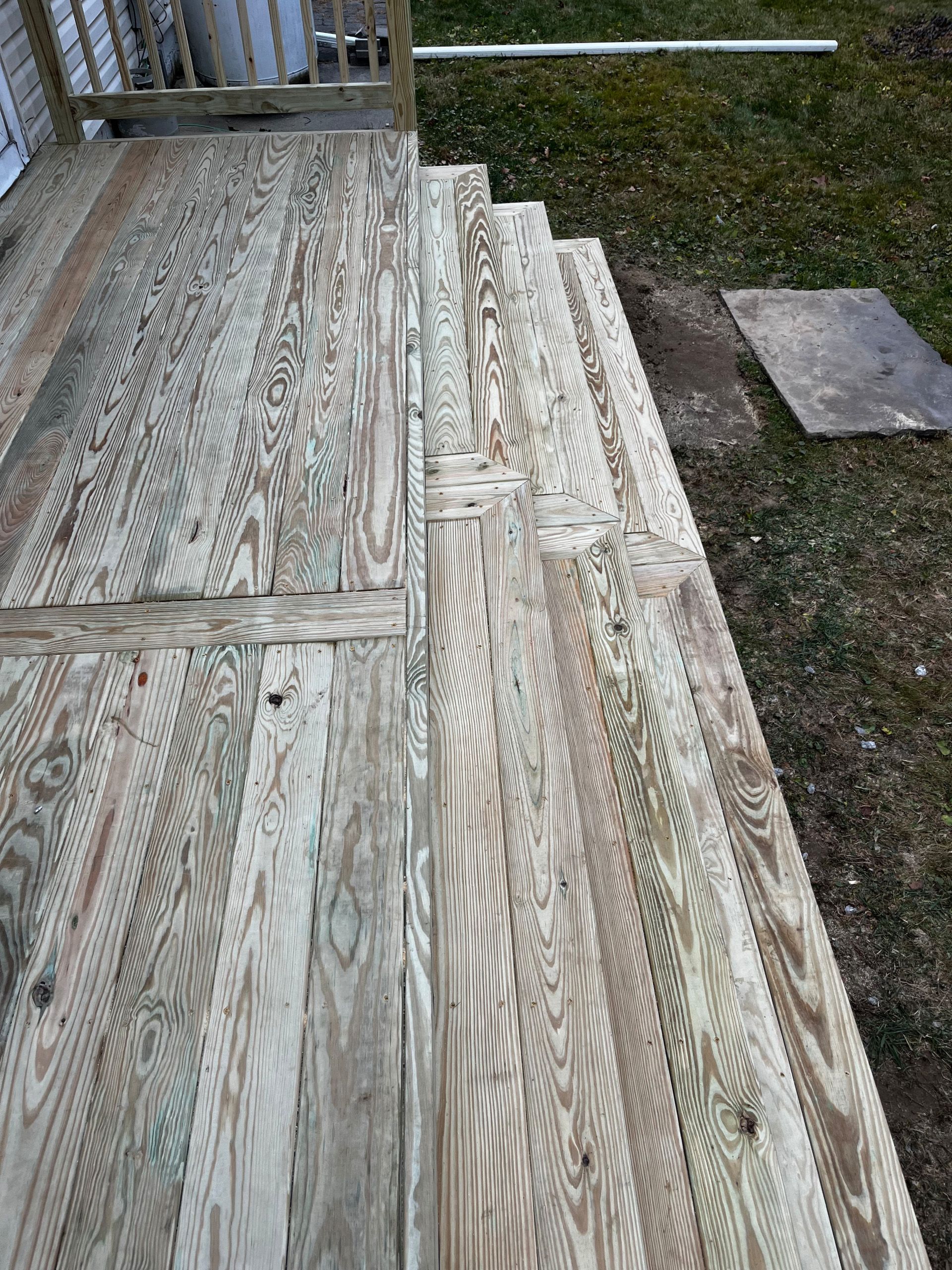 Wooden deck with steps leading down to grass, gray weathered wood.