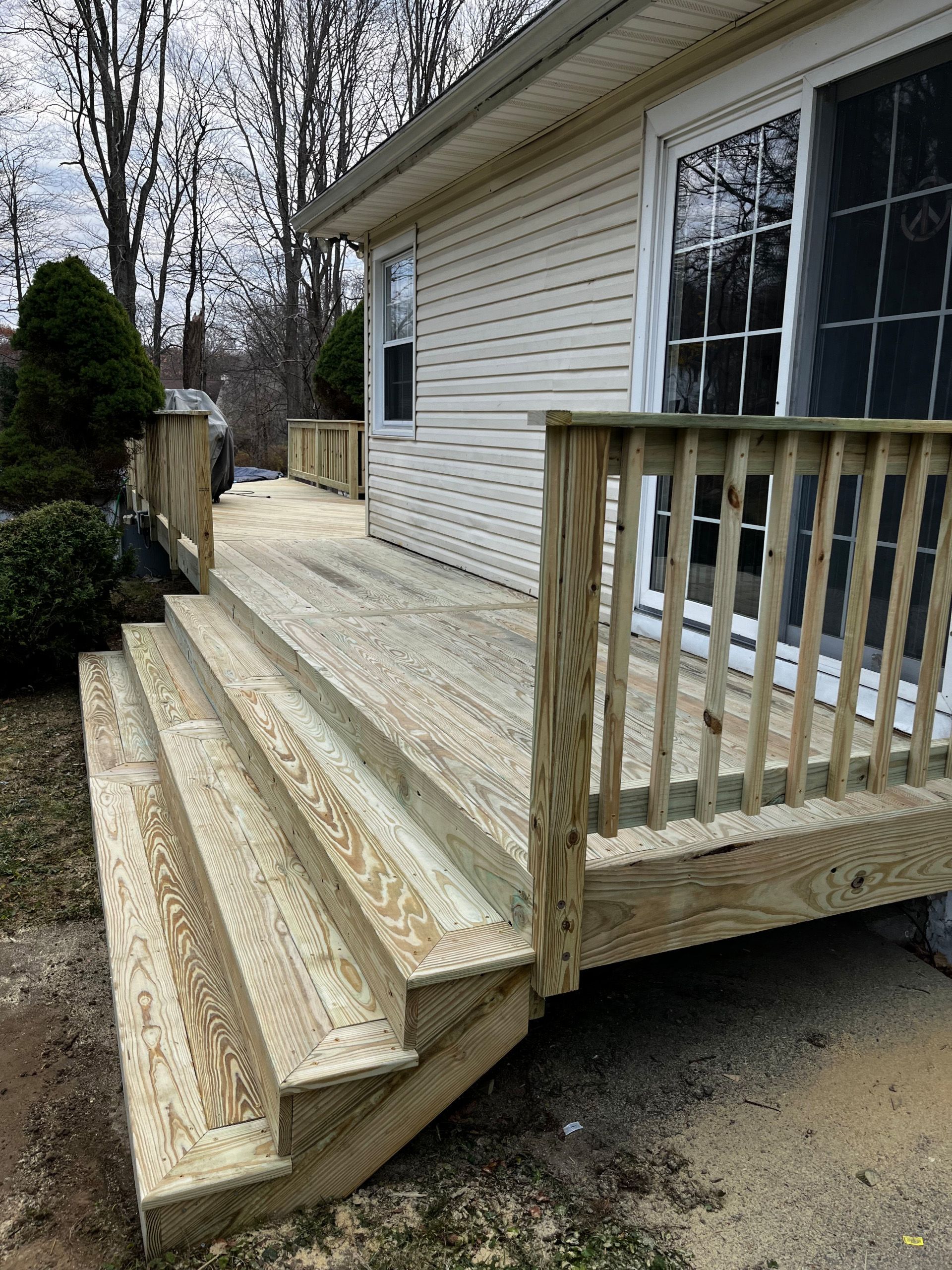 Wooden deck with steps leading up to a house with sliding glass door, and railing.