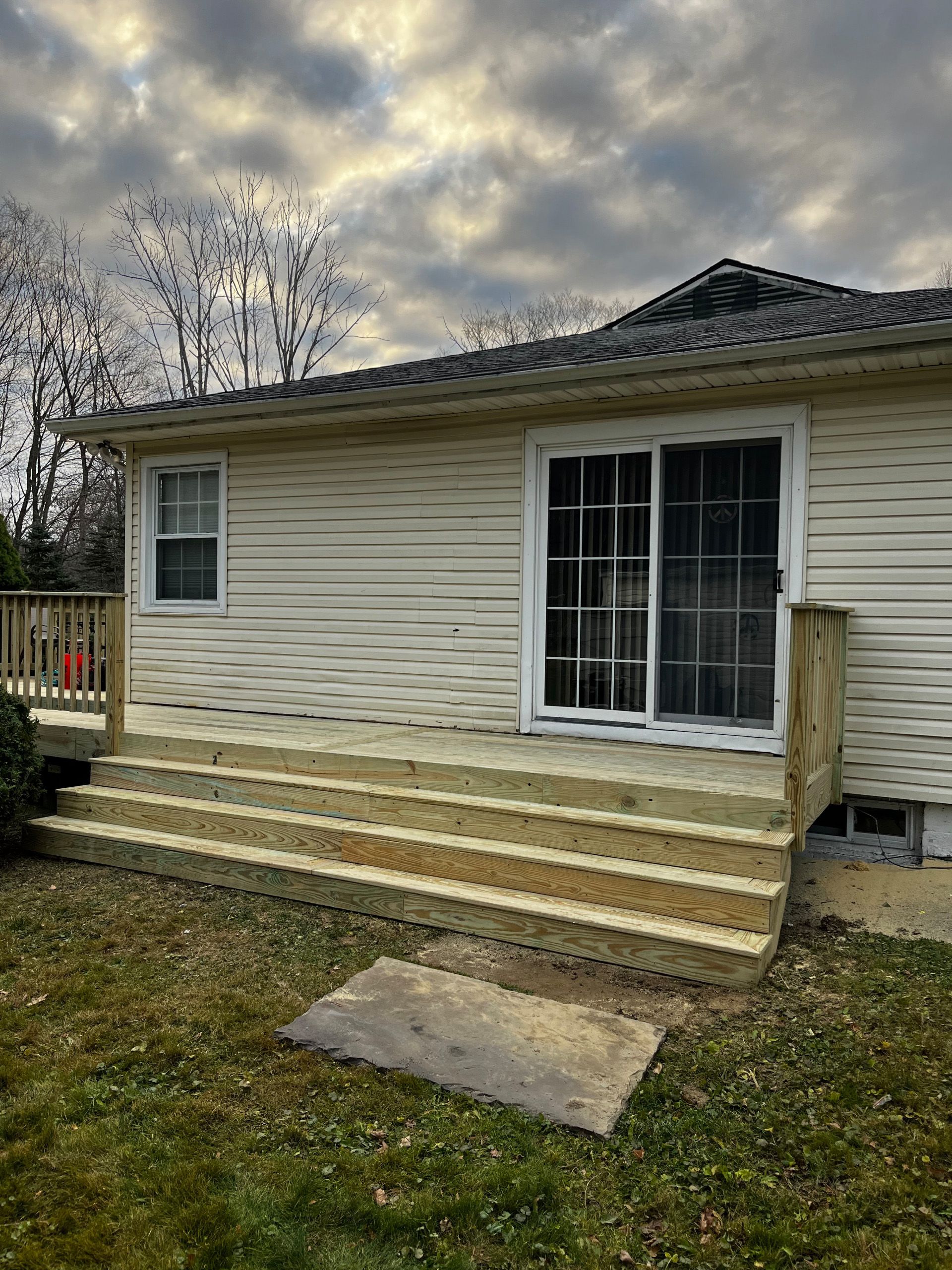 Wooden deck with steps leading to a sliding glass door of a house, with cloudy sky above.