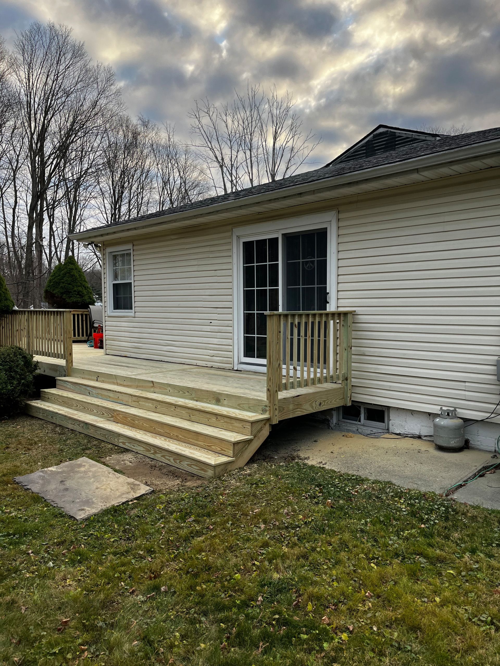 New wooden deck with steps leading to a sliding glass door on the side of a house.