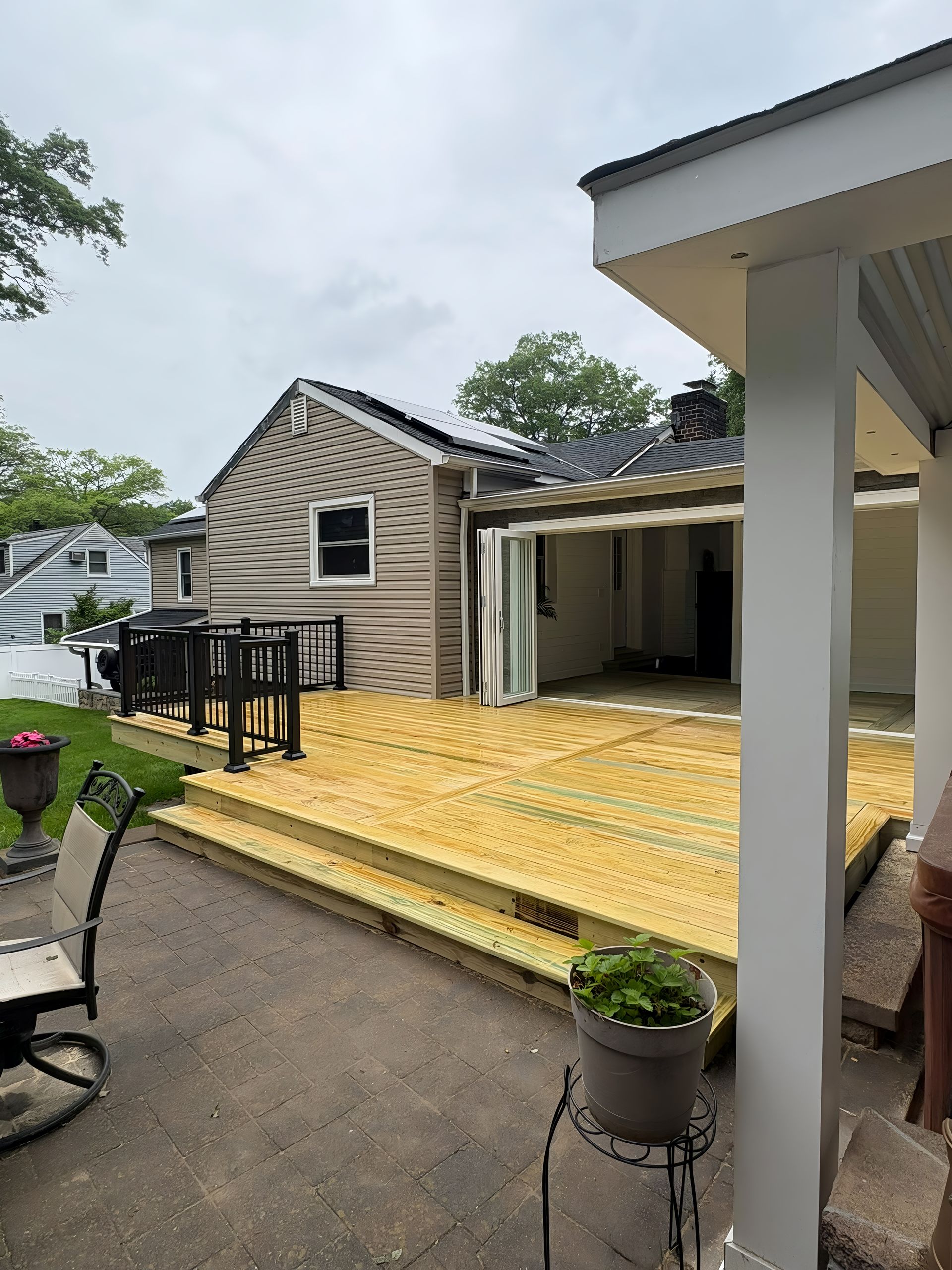 Wooden deck with black railing; back of a tan house; patio furniture on patio.
