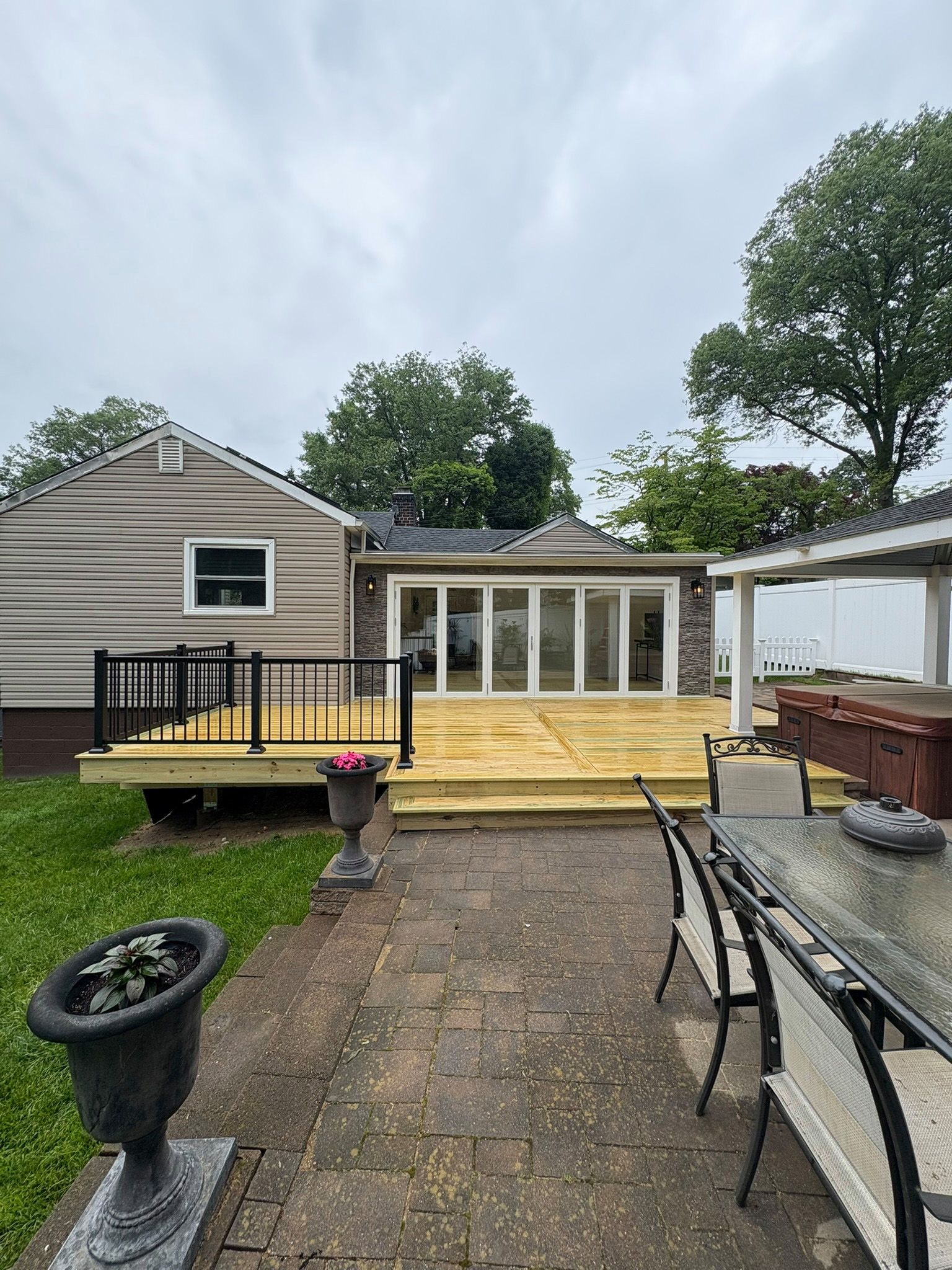 Backyard with a deck, brick patio, and a home featuring a glass wall and a white pergola.
