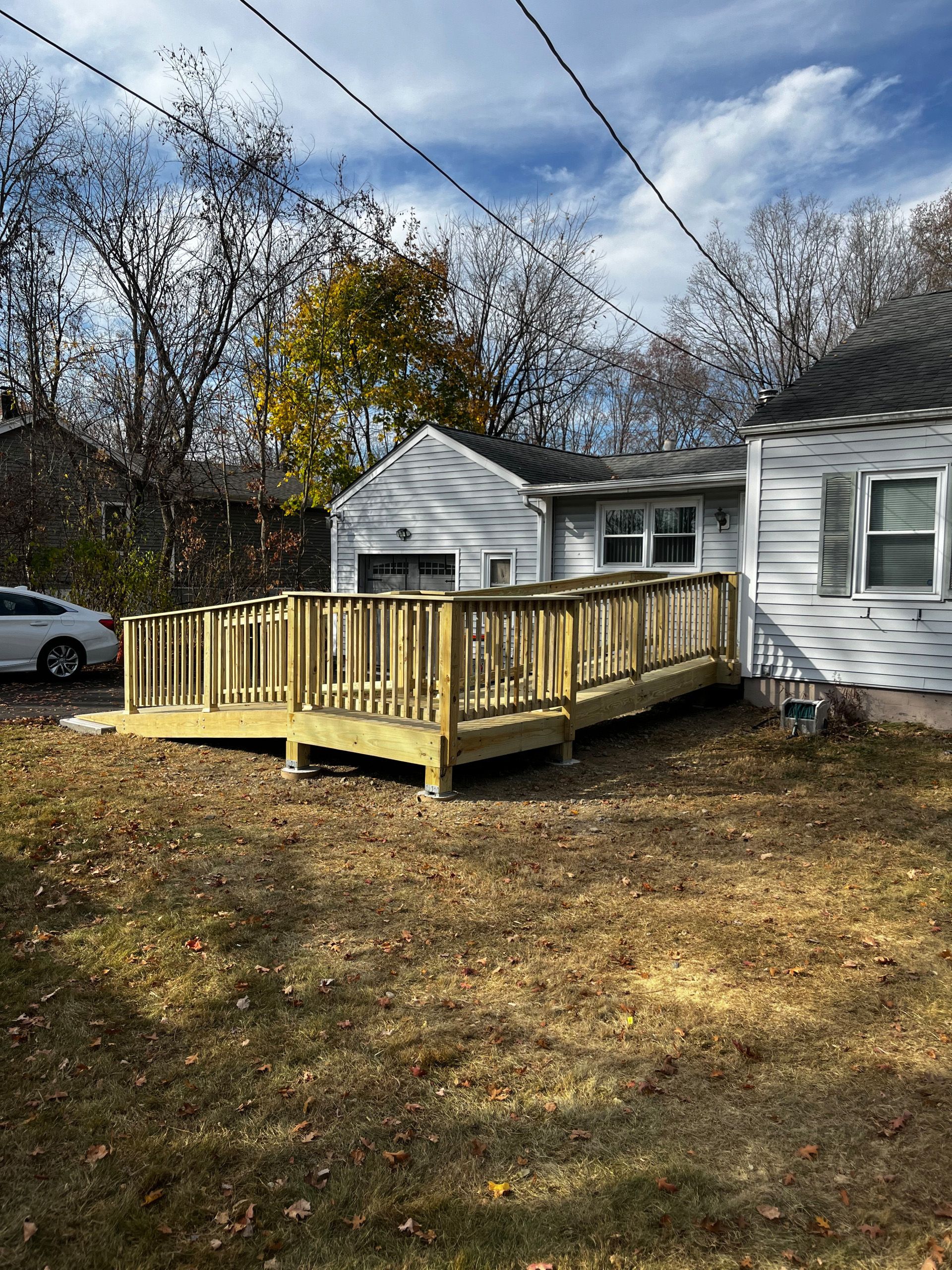 Wooden ramp and deck attached to a light gray house with a garage, on a sunny day.