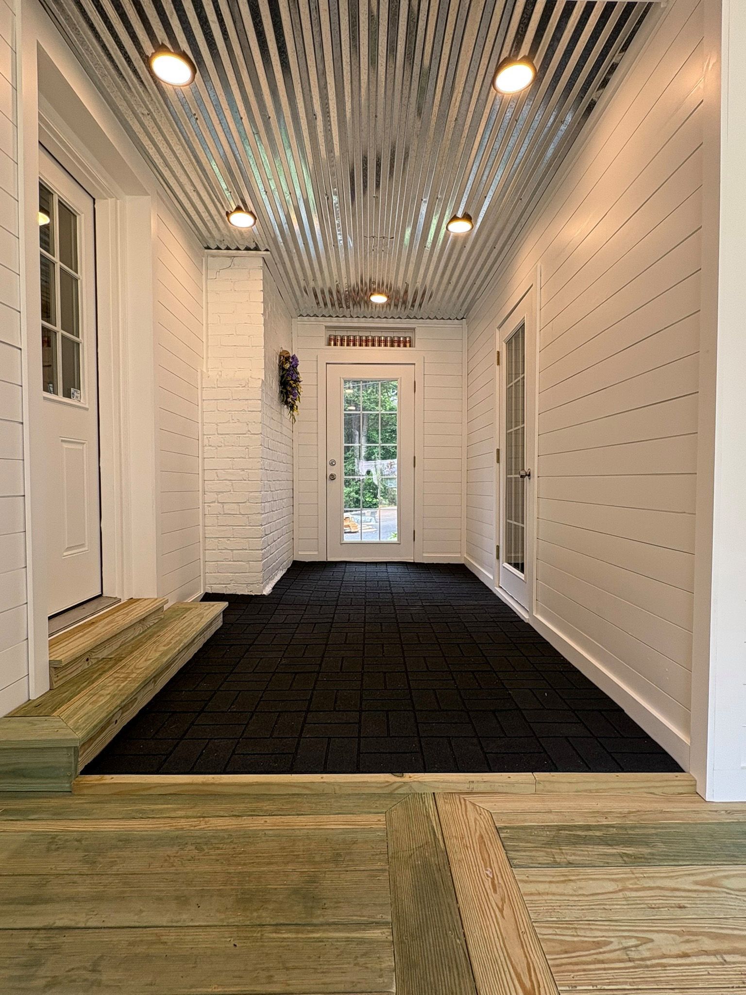 White porch entryway with black flooring, metal ceiling, and glass doors.